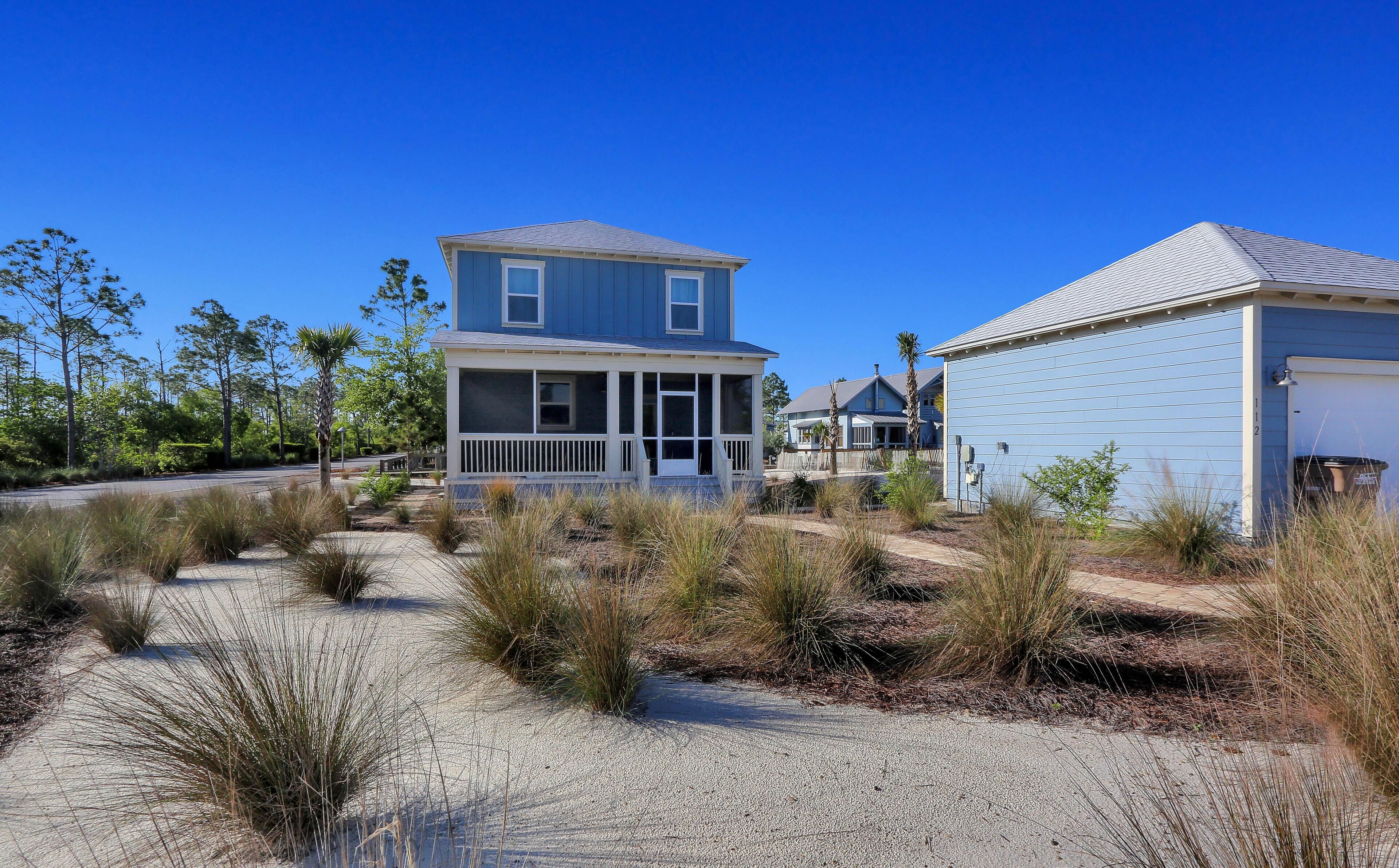 A two-story house with a porch, surrounded by dry grass and trees.