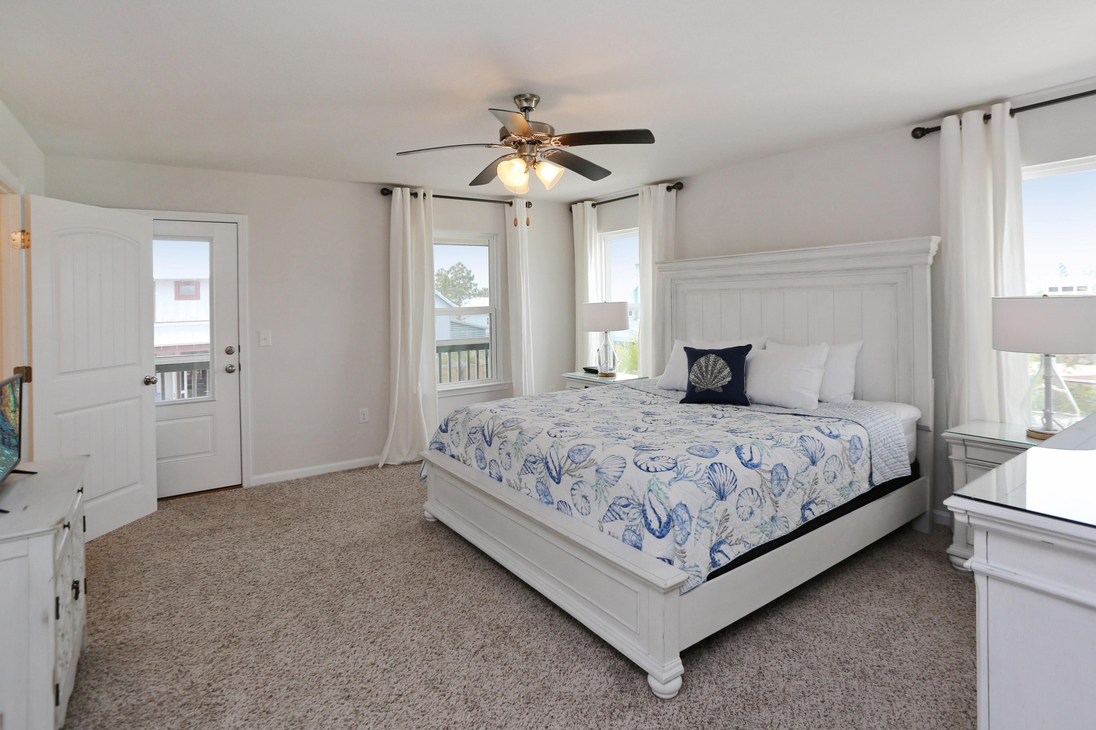 A bedroom with a bed, a ceiling fan, a window with curtains, and a door.