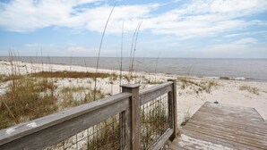 Ein hölzerner Steg führt zu einem Sandstrand mit Blick auf das Meer.
