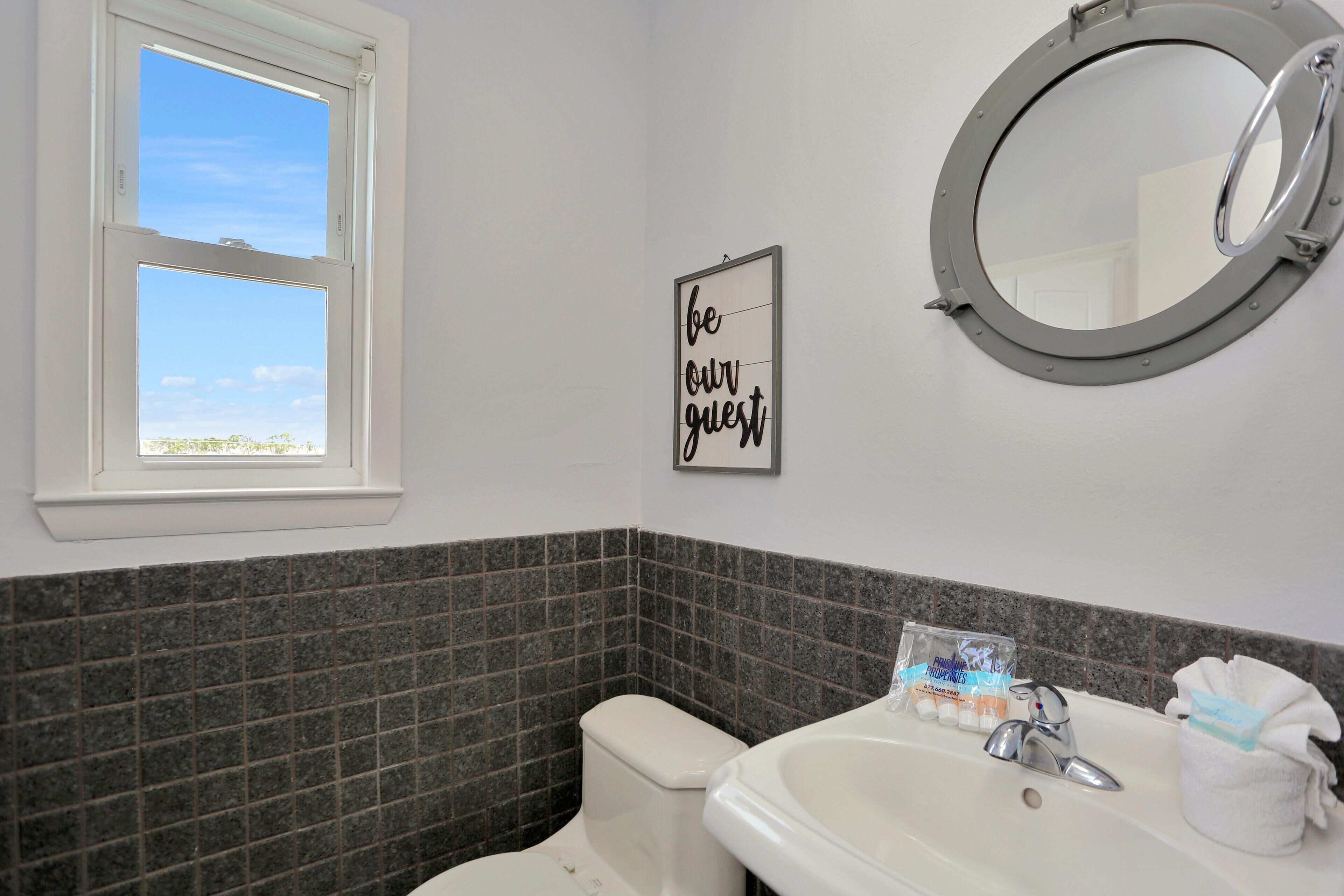 A bathroom with a toilet, sink, and a window with a view of the sky.