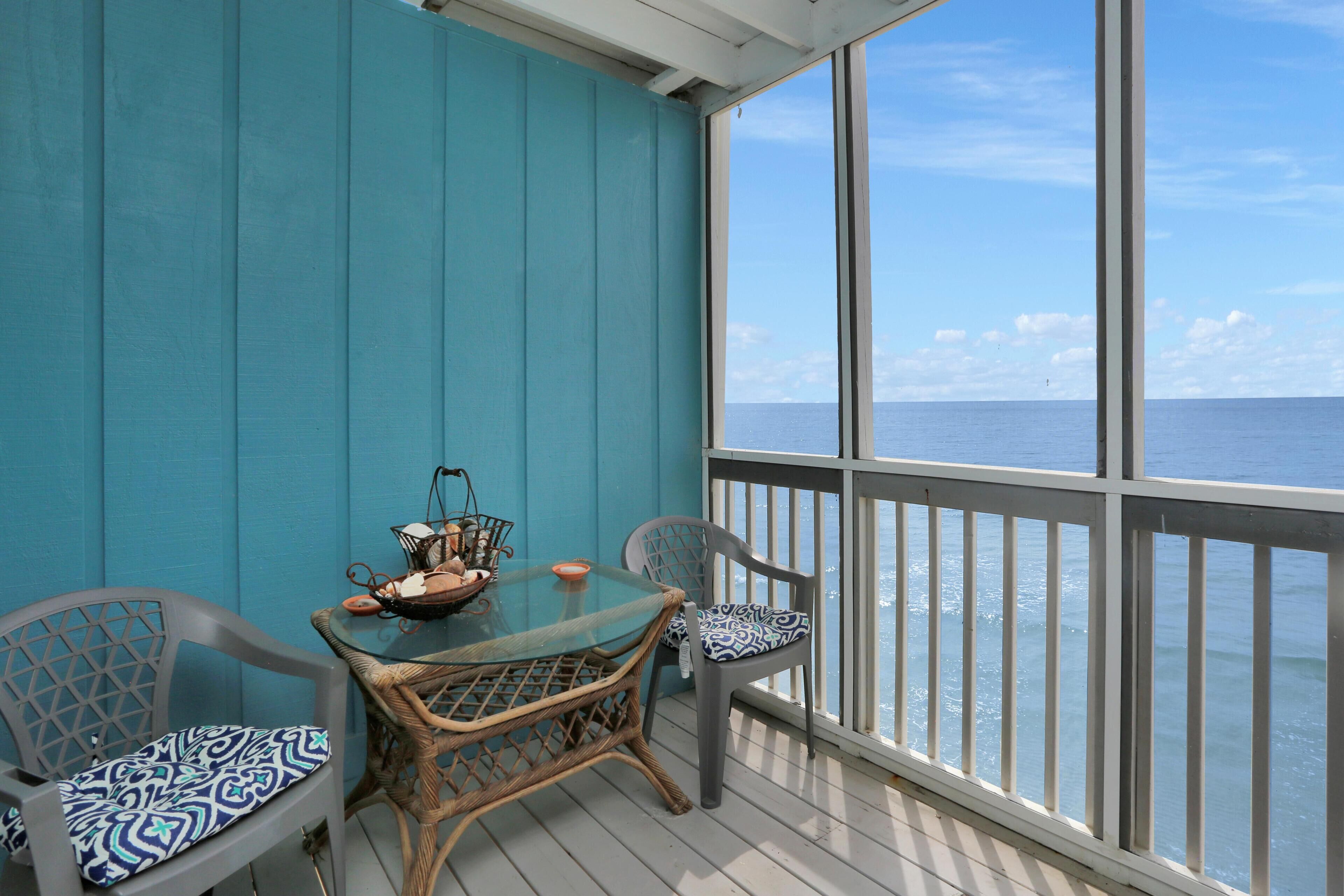 Un balcon avec une table en verre et des chaises en osier, donnant sur la mer.
