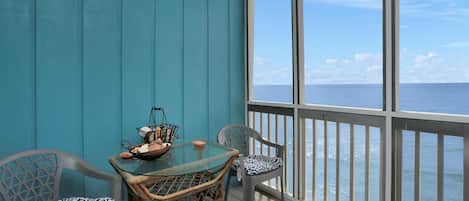 Un balcon avec une table en verre et des chaises en osier, donnant sur la mer.