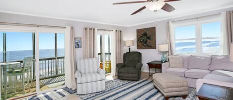A spacious living room with a balcony, a ceiling fan, a sofa, a chair, and a view of the ocean.