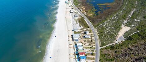 An aerial view of a coastal area with a beach, a road, and scattered buildings.