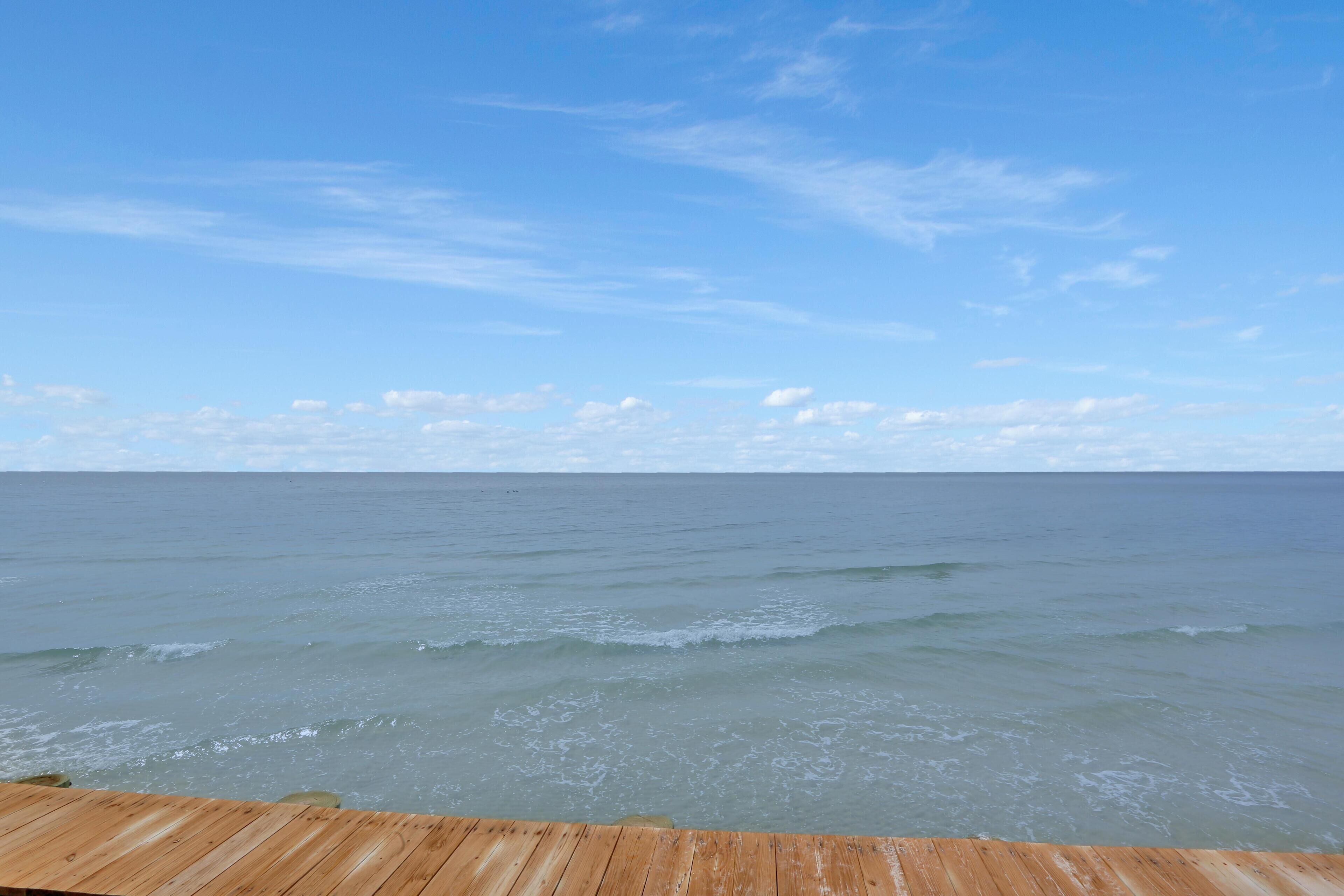 Une terrasse en bois donnant sur une mer calme, sous un ciel dégagé.