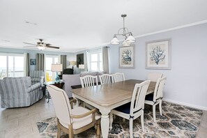 A dining area with a wooden table and white chairs, a ceiling fan, and artwork on the walls.