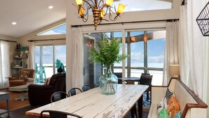 A dining area with a wooden table, chairs, a vase with greenery, and a view through large windows. - WindScape (Port St. Joe)