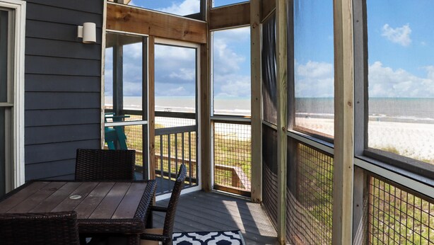 A covered outdoor area with a wooden deck, wicker furniture, and a view of the beach. - WindScape (Port St. Joe)