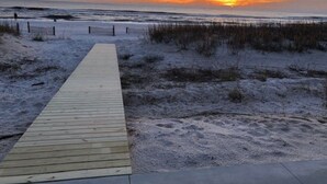 Une promenade en bois menant à une plage, avec un coucher de soleil en arrière-plan.