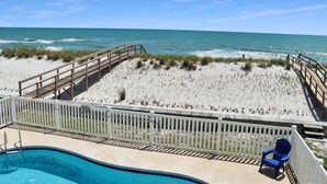 A beach view with a wooden deck, a pool, and a white fence.