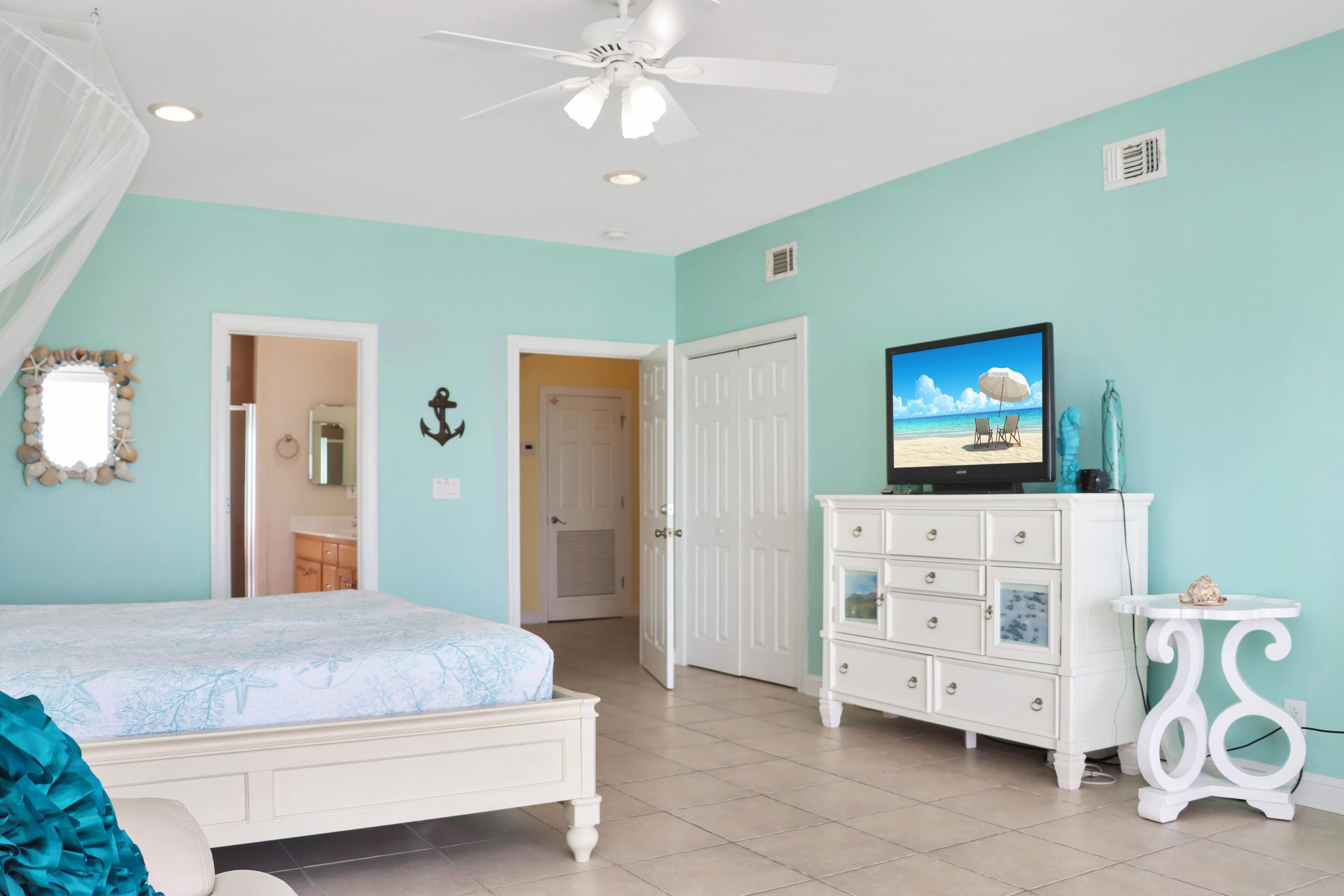 A bedroom with a bed, a dresser, a television, and a ceiling fan.