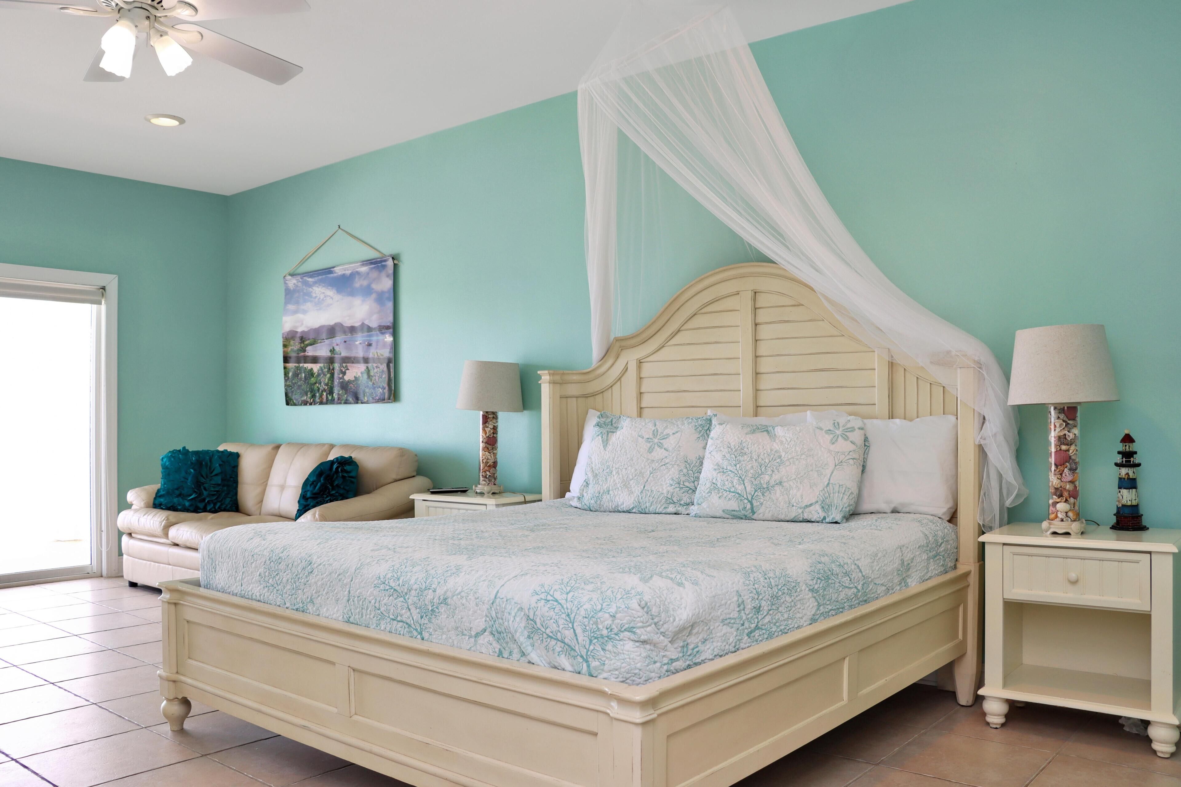 A bedroom with a bed, nightstands, a ceiling fan, a window, and a wall-mounted artwork.