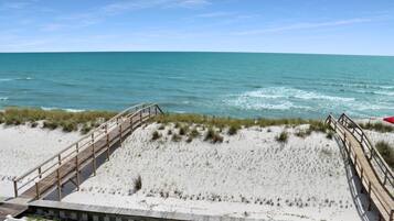 Une plage avec une promenade en bois qui mène à l’eau, une plage de sable et un ciel bleu clair.