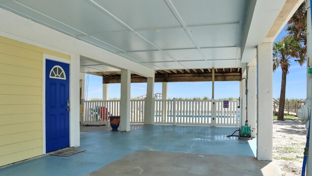 A covered outdoor area with a blue door, white fence, and a concrete floor.