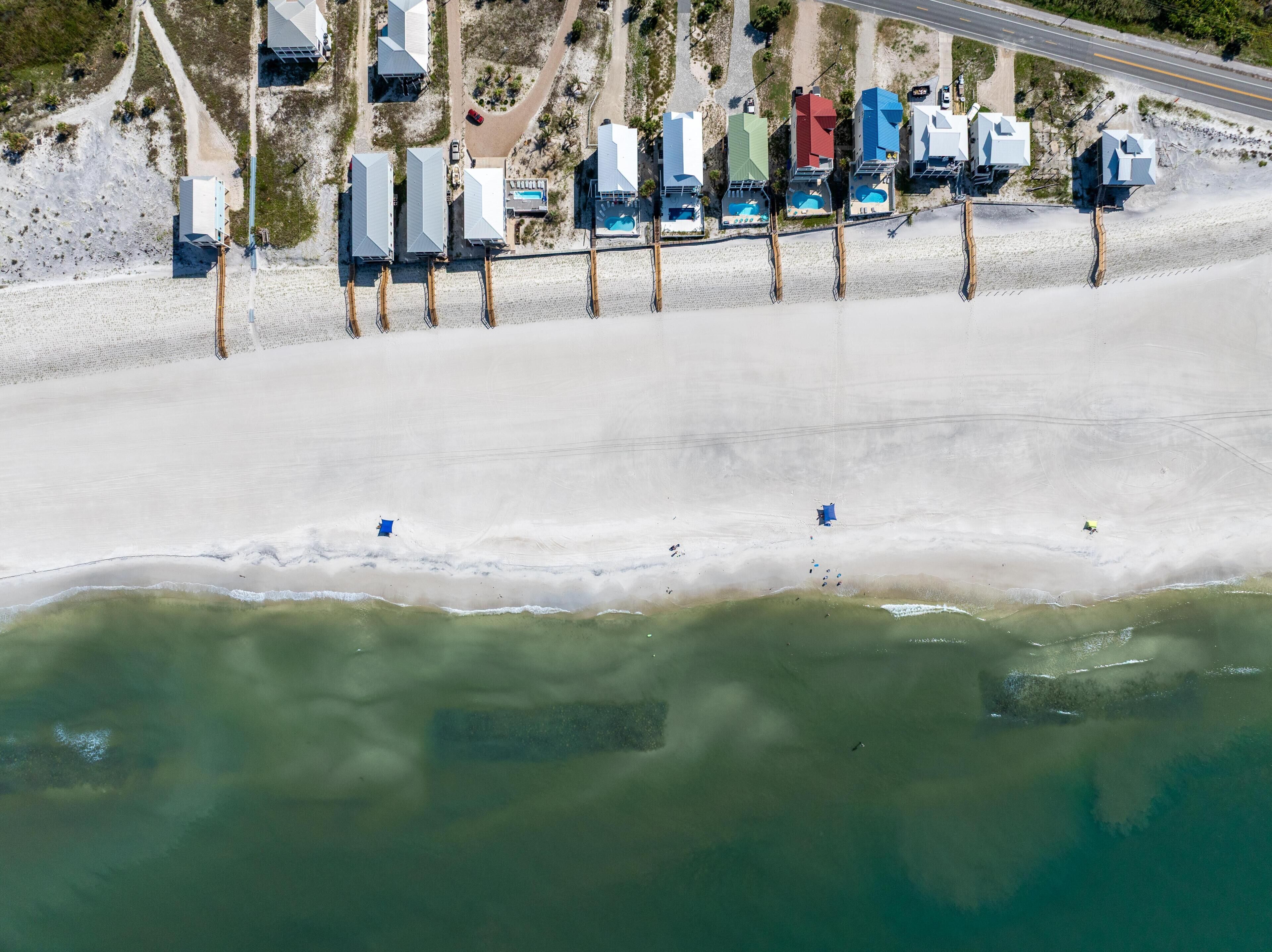 An aerial view of a beachside hotel with multiple buildings, a swimming pool, and a road parallel to the beach.
