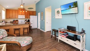 A living room with a sofa, a TV, and a coffee table. There is a kitchen area with wooden cabinets and a microwave. - Sweet Destiny (Port St. Joe)