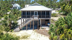 A beachfront house with a balcony, a staircase leading to the deck, and a sandy beach in the background. - Sweet Destiny (Port St. Joe)