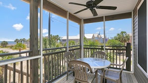 A covered outdoor area with a table and chairs, a ceiling fan, and a view of the beach and buildings. - Sweet Destiny (Port St. Joe)