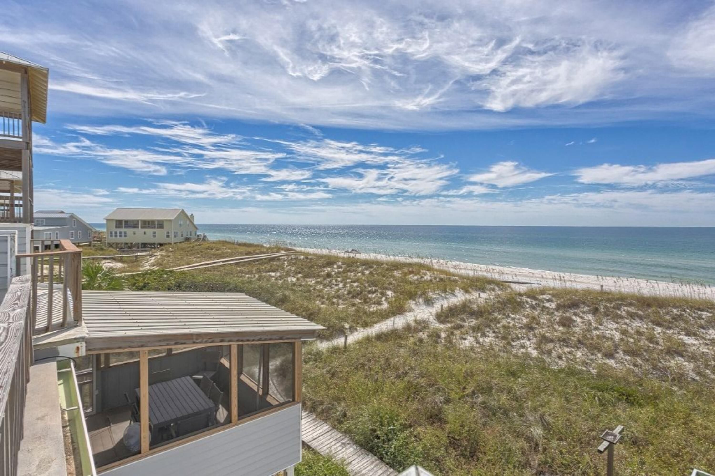 A beachfront property with a wooden deck, a glass-enclosed room, and a view of the ocean and beach.