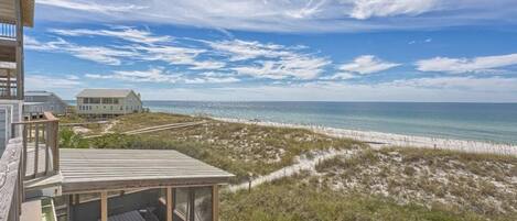 A beachfront property with a wooden deck, a glass-enclosed room, and a view of the ocean and beach.