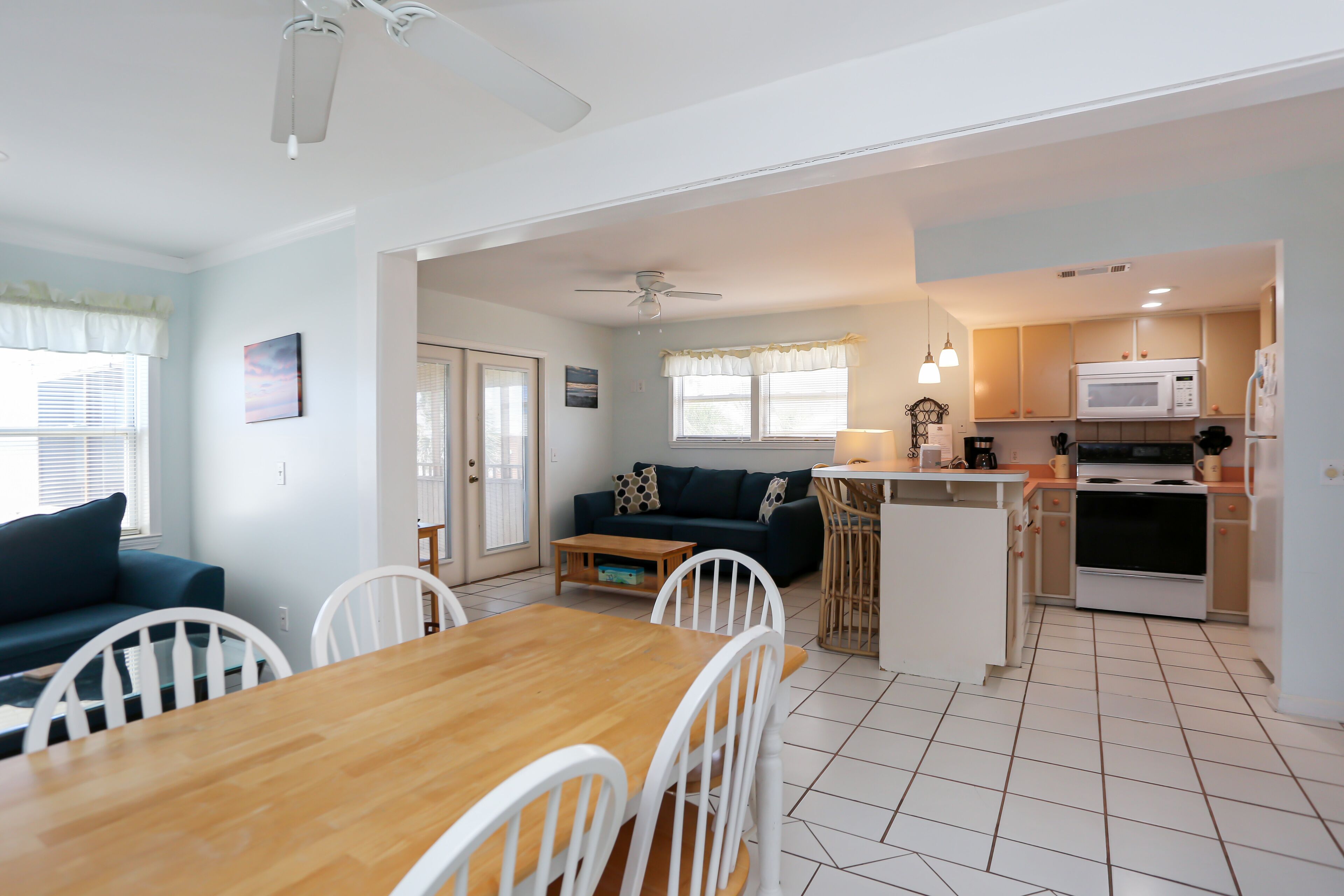 A modern kitchen with white cabinets, a microwave, and a stove. There is a dining area with a wooden table and white chairs.