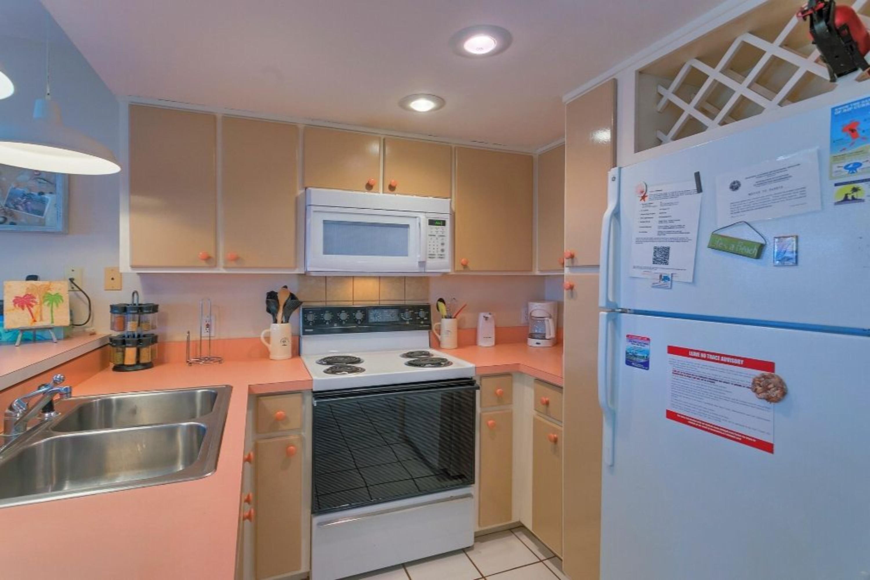 Una cocina compacta equipada con microondas, estufa y refrigerador, con cubierta rosa y armarios color beige.