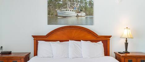 Uma cama bem arrumada com lençóis brancos, cabeceira de madeira e mesa de cabeceira com abajur.