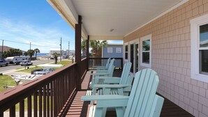 A covered porch with light blue Adirondack chairs, a view of the street, and a building with a light blue exterior. - The Shore House (Port St. Joe)
