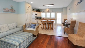 A spacious living area with a sofa, wicker chairs, a dining table, and a kitchen in the background. - The Shore House (Port St. Joe)