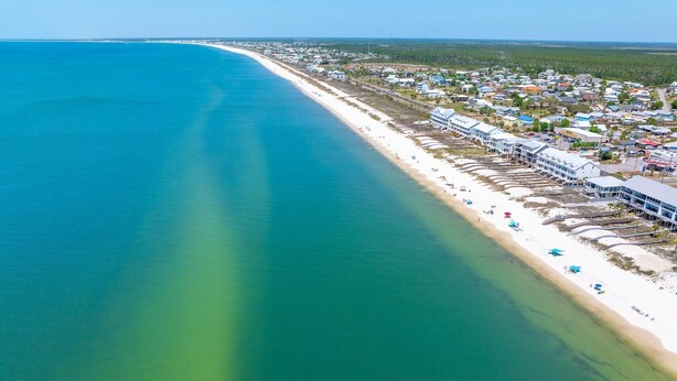 An aerial view of a coastal area with a beach, buildings, and a clear blue sea. - The Shore House (Port St. Joe)