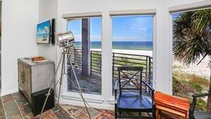 Un balcone con vista sull'oceano, un treppiede, una sedia e un piccolo armadietto.