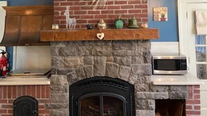 Ein Kamin mit Steinverkleidung und einer schwarzen Glasfront, ein Holzbodenbrett mit Dekorationen sowie eine Mikrowelle auf der angrenzenden Arbeitsfläche.