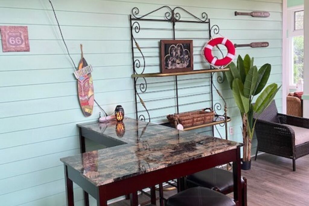 Un coin repas avec une table en marbre, une étagère en métal ornée d’objets décoratifs, un gilet de sauvetage et une chaise en osier.
