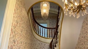 Eine prächtige Treppe mit hölzerner Handläufung, einem Chandelier und blumigem Wandpapier.