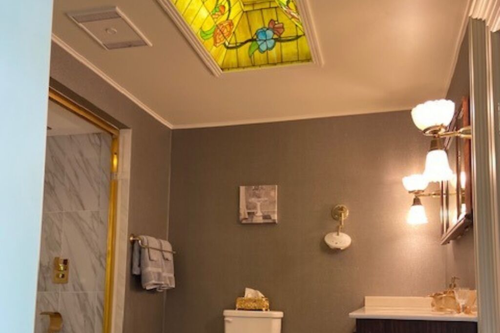 Une salle de bain avec un mur en marbre, des toilettes, un lavabo avec un miroir et une fenêtre à vitraux au-dessus du lavabo.