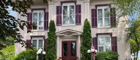 A stately two-story house with a symmetrical facade, a central entrance with a double door, and a front porch with steps leading up to it.