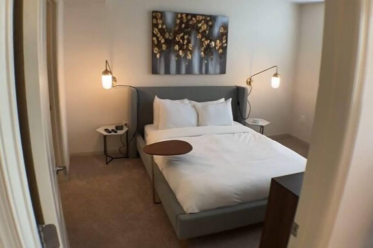 A modern hotel room with a bed, bedside tables, and a painting on the wall.