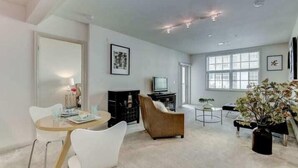 A spacious living room with a round wooden table, white chairs, a brown sofa, and a television on a black stand. - National at Clarendon (Arlington)