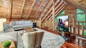 Ein großzügiger Loftsitz mit hohen Decken, Holzbalken, einem großen Flachbildfernseher, einem Sofa, einem Sessel und einem Couchtisch.