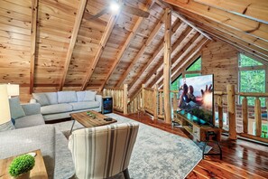 Un loft spacieux avec un plafond haut, des poutres apparentes, un grand téléviseur à écran plat, un canapé, un fauteuil et une table basse.