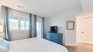 Ein Schlafzimmer mit einem großen Bett, einem Schminktisch, einem Fernseher und einem Fenster mit Vorhängen.