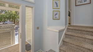 Eine Treppe mit einem mit Teppich belegten Geländer, das zu einer Zwischenebene führt. Über der Treppe hängen drei gerahmte Bilder an der Wand.