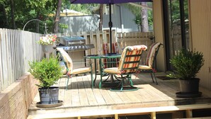 Une terrasse en bois avec une table et des chaises, un barbecue et des plantes en pot.