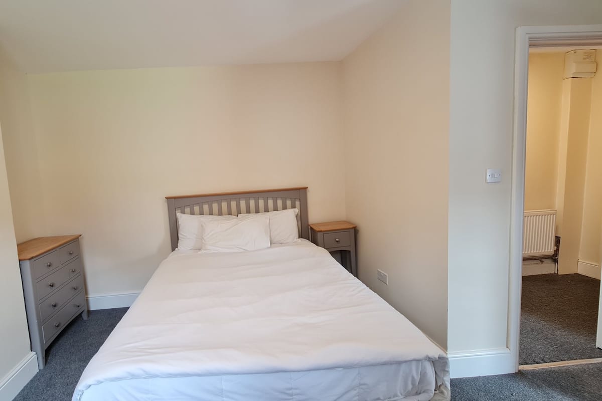 Une chambre avec un lit simple, une table de chevet, une commode et un radiateur.
