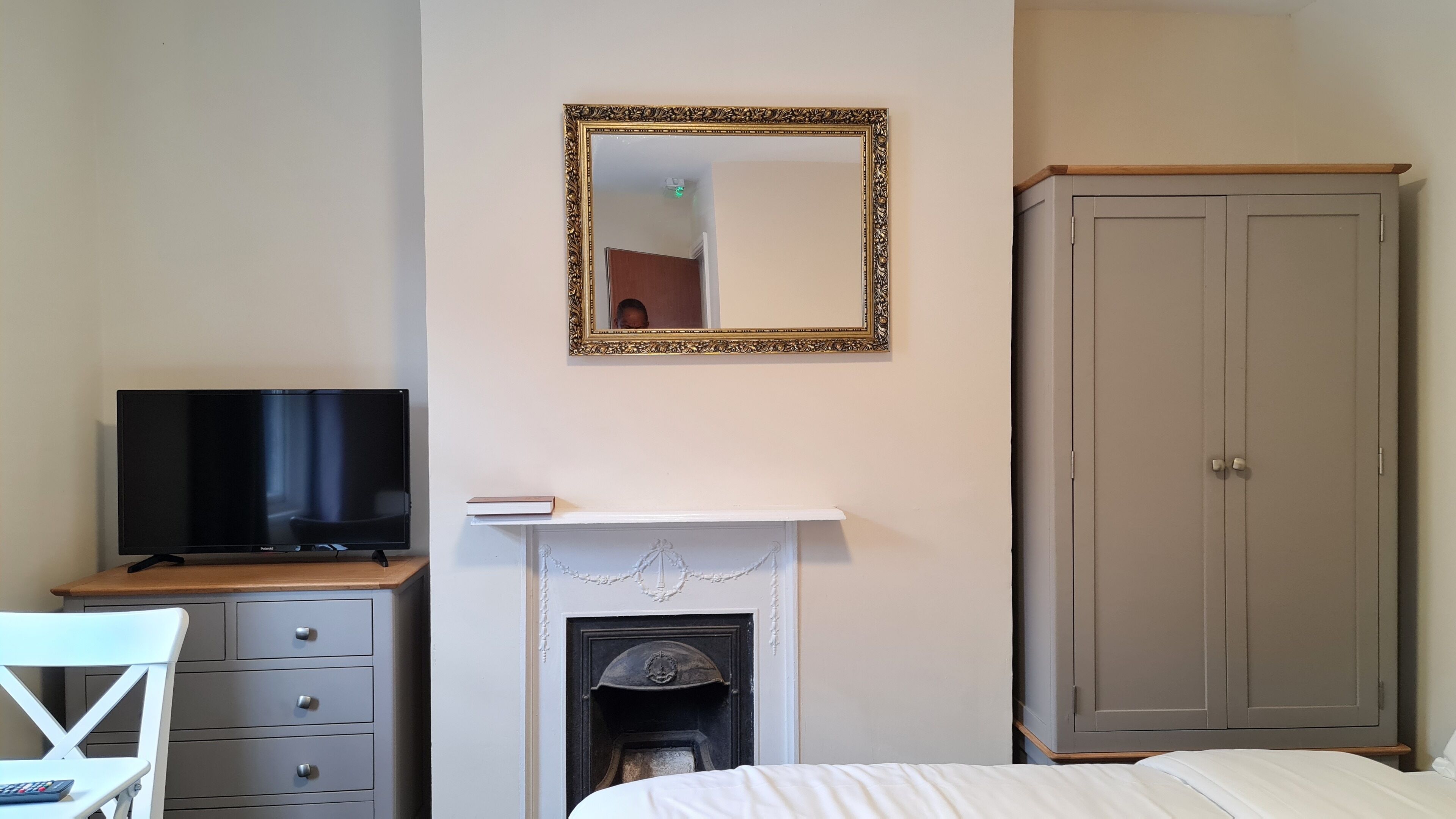 A bedroom with a television, a fireplace, a wardrobe, and a mirror.