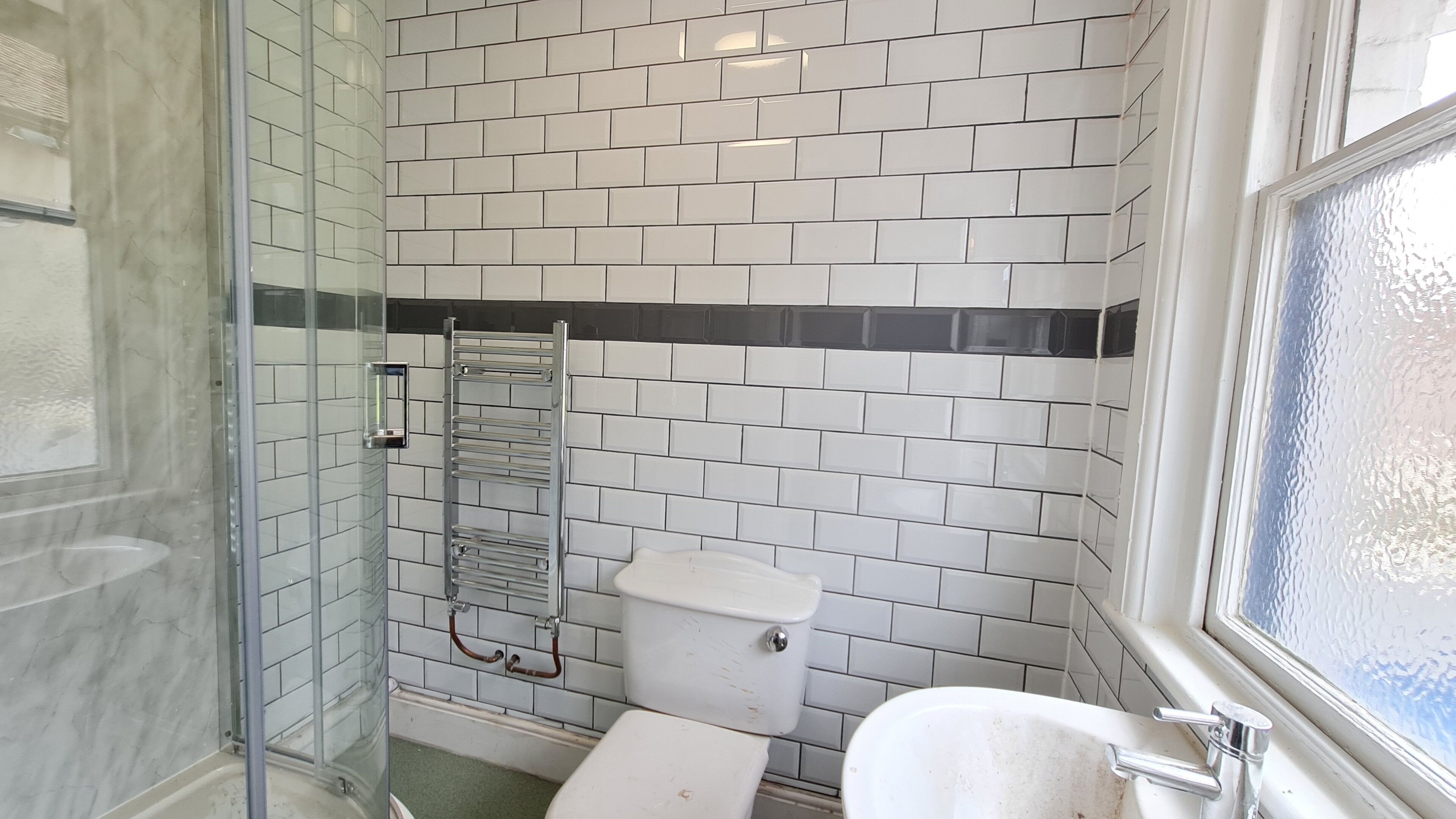 A bathroom with white subway tiles, a glass shower enclosure, a toilet, and a sink.