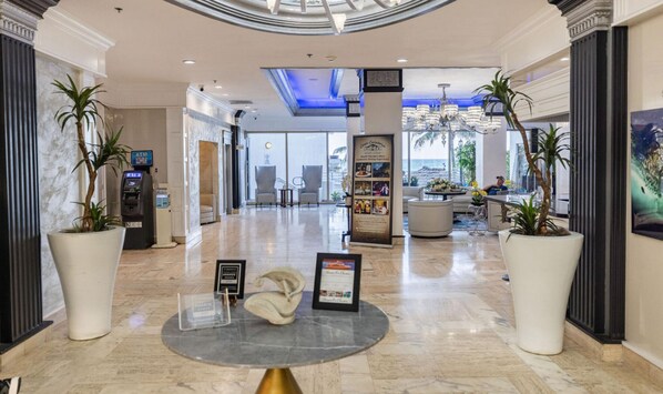 A hotel lobby with a marble floor, a reception desk, a seating area, and a view of the ocean.