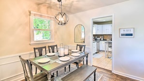 A dining area with a table set for six, a chandelier, and a kitchen visible through an open doorway. - Charming Hampton Home w/ Yard: 2 Mi to Beach! (Hampton)