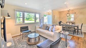 A spacious living room with a large window, a sofa, a coffee table, and a dining area with a table and chairs. - Charming Hampton Home w/ Yard: 2 Mi to Beach! (Hampton)