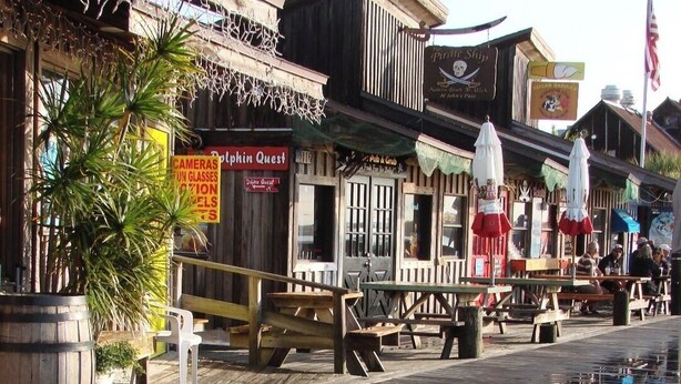 Une promenade en bois bordée de boutiques et d’un panneau indiquant le restaurant « Pirate Ship ».